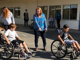 teachers helping students in wheelchairs outside