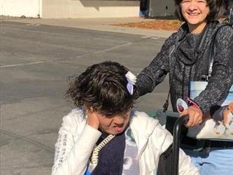 student helping push a student in a wheelchair outside